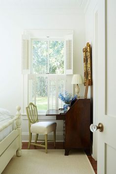 a bedroom with a bed, desk and chair next to a window that has shutters