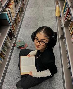 a woman sitting on the floor reading a book in a library with bookshelves behind her