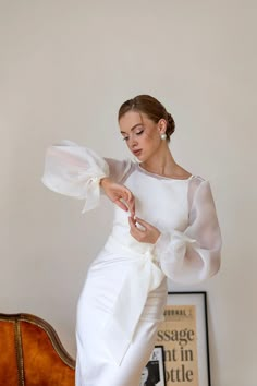 a woman in a white dress is standing on a chair and looking down at her hand