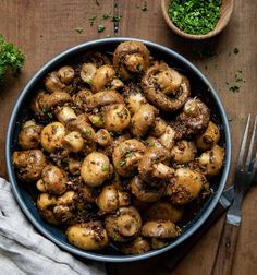 a bowl filled with cooked mushrooms next to a fork and napkin on top of a wooden table