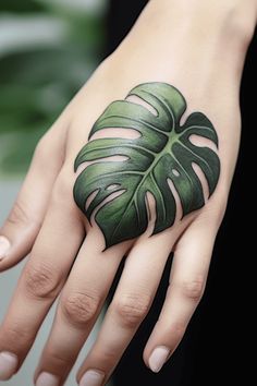 a woman's hand with a green leaf tattoo on it