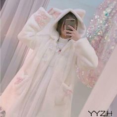 a woman taking a selfie in front of a mirror wearing a white teddy bear coat