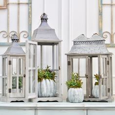 three white pumpkin shaped lanterns sitting on top of a table next to each other with plants in them