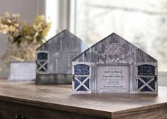 three small wooden barn shaped houses sitting on top of a table next to a vase with flowers