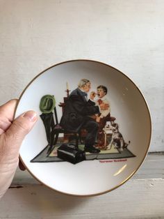 a hand holding a plate with an image of two men and a dog on it