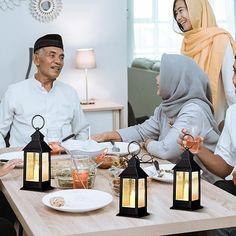 a group of people sitting around a wooden table with lanterns on top of it and plates in front of them