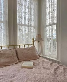 a bed sitting in front of two windows with curtains on each side and a book laying on top of it