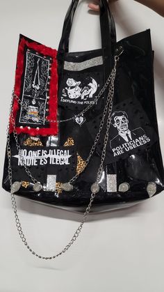 a hand holding a black bag with red and white patches on it, which is attached to a chain