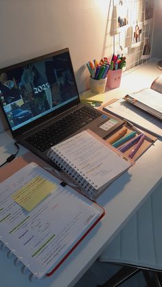 an open laptop computer sitting on top of a desk next to a notebook and pencils