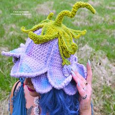 a woman with blue hair wearing a crocheted hat and holding her hand up to her face