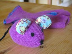 a purple knitted mouse with flowers on it's ears sitting on top of a wooden table