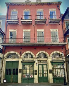 an old building with green doors and balconies on the second floor is painted red