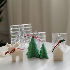 three small plastic christmas trees on top of a white table next to a house ornament