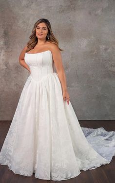 a woman in a white wedding dress standing on a wooden floor with her arms behind her back