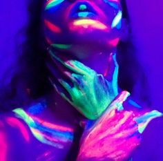 a woman with her hands on her chest and face painted in neon colors, posing for the camera