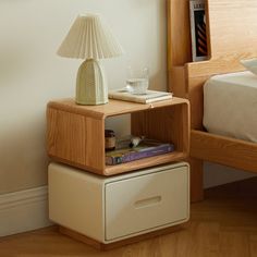 a nightstand with a lamp on top of it next to a bed