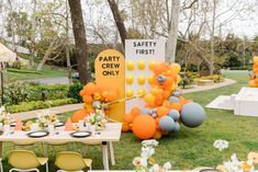 an outdoor party with orange and gray balloons, white tablecloths and yellow chairs