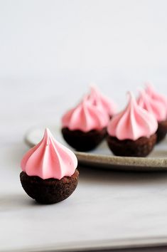 three chocolate cupcakes with pink frosting on a plate next to another one