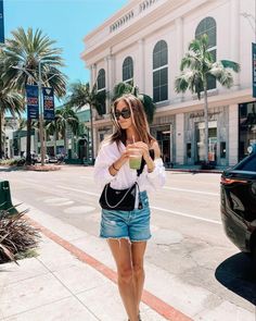 a woman walking down the street while holding a drink