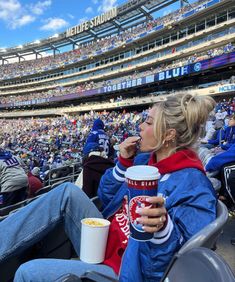 a woman sitting in the stands at a football game eating and drinking from a cup