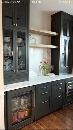 an empty kitchen with black cabinets and white counter tops is pictured in this image, there are two wine glasses on the cabinet doors