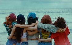 four girls standing together on the beach with their arms around each other's shoulders