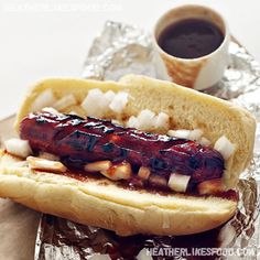 a hot dog with onions and ketchup on a piece of tin foil next to a cup of coffee