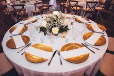 the table is set with white and gold plates, silverware, and flower centerpieces