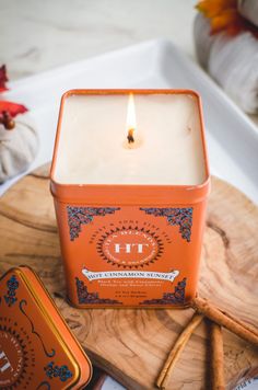 an orange candle sitting on top of a wooden tray next to some cinnamon sticks and other items