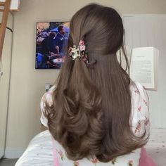 the back of a woman's head with long brown hair and flowers in her hair