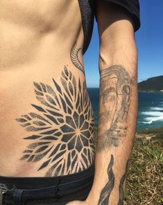 a man with tattoos on his stomach standing next to the ocean