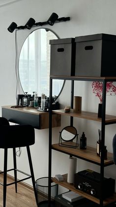 a room with a desk, mirror and stools in front of a window that has a circular mirror on the wall above it