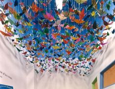 a room filled with lots of origami birds hanging from the ceiling above it