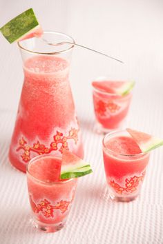 watermelon drink in glasses and pitcher on white tablecloth with green stick sticking out of top