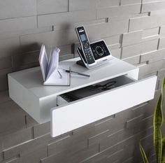 two cell phones are sitting on top of a white shelf next to an open book