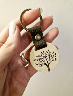 a hand holding a wooden keychain with a tree on it