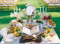 an open book sitting on top of a table covered in flowers and other items next to a mirror