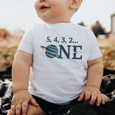 a baby sitting on top of a blanket wearing a shirt that says 5, 3, 2 one