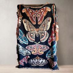 a blanket with moths on it and tassels hanging from the side, in front of a wall