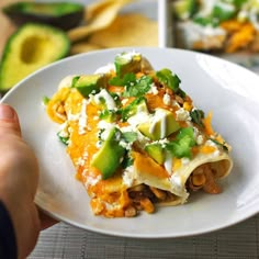 a person holding a plate with mexican food on it and an avocado in the background