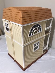 a doll house is sitting on top of a white bed sheet with a brown roof