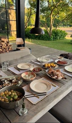 an outdoor dining table set with plates and bowls full of food on top of it