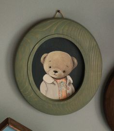 a painting of a teddy bear in a green frame on the wall next to a clock