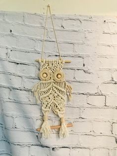 a crocheted owl hanging on a brick wall in front of a white brick wall