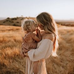 a woman holding a baby in her arms while standing in a field with tall grass