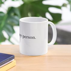 a white coffee mug sitting on top of a wooden table next to a blue book