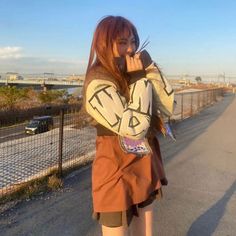 a woman standing on the side of a road talking on a cell phone while holding onto her arm