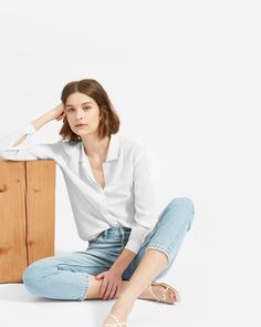 a woman sitting on the ground with her legs crossed, wearing jeans and a white shirt