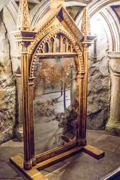 an ornate wooden mirror on display in a stone walled room with columns and arches around it