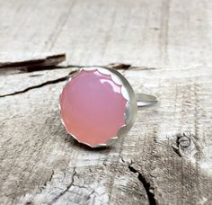 A lovely round blush pink or aqua blue chalcedony has been set in sterling silver and is framed by an elegant scallop setting. The ring band has been handmade from sterling silver half dome wire. The chalcedony is 20mm in size. The ring is chic and easy to wear with any outfit!Also available in a simple plain setting, see photo three in both stone colors!Made to order! Pink Moonstone Ring Gift, Pink Round Moonstone Ring For Gift, Adjustable Pink Moonstone Round Ring, Adjustable Pink Moonstone Ring, Adjustable Pink Round Moonstone Ring, Round Pink Opal Moonstone Ring Gift, Pink Chalcedony, Blue Or Pink, Ring Blue